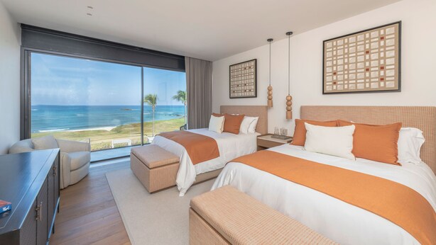Une chambre d’hôtel avec deux lits, un bureau et une grande fenêtre donnant sur l’océan.