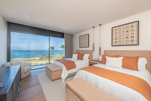 Quarto de hotel com duas camas, uma escrivaninha e uma janela grande com vista para o oceano.