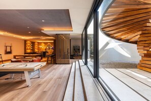 Um interior moderno com mesa de bilhar, piso de madeira e vista para o exterior.
