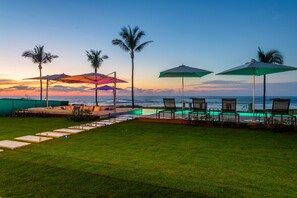 A poolside area with lounge chairs and umbrellas, palm trees, and a view of the ocean at sunset. - Punta Pac Fico 7 in Punta Mita (Punta de Mita)