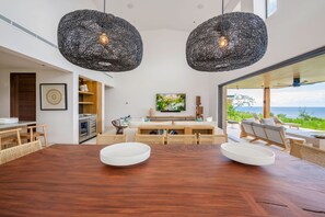 Ein moderner Essbereich mit einem Holztisch, zwei weißen Schüsseln, Korbstühlen und einem großen Fenster mit Blick auf eine schöne Landschaft.