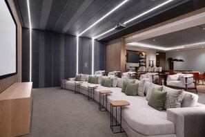 Eine moderne Lounge mit einer gebogenen Couch, kleinen Tischen und einer Projektionsleinwand.