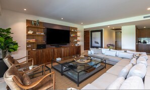 Un salon moderne avec un téléviseur à écran plat, des étagères en bois, une table basse en verre et un canapé.