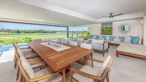Un espace de restauration extérieur moderne, avec une table et des chaises en bois, un ensemble de canapés et une vue sur un terrain de golf.