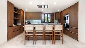 Une cuisine moderne avec des meubles en bois, un îlot central doté de chaises, un four à micro-ondes encastré et une grande fenêtre.
