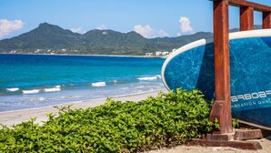 A beach with a wooden structure, a clear blue sea, and a mountain in the background. - Penthouse Tau Prima Vista (Punta de Mita)