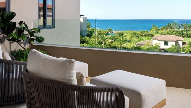 A balcony with wicker furniture, a view of the ocean, and a building with a tiled roof. - Penthouse Tau Prima Vista (Punta de Mita)
