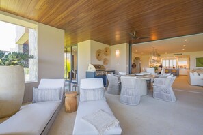 Ein zeitgemäßer Außenbereich mit Holzboden, weißen Sofas, Korbstühlen und einer Küche im Hintergrund.