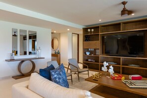 Ein modernes Wohnzimmer mit einer Couch, Sesseln, einem Couchtisch, einem Fernseher und einem Bücherregal.