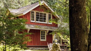 A red wooden house with a stone staircase leading to the front door, surrounded by trees. - Waterfront lodge on 24 acres with patio & fireplace (Rhododendron)