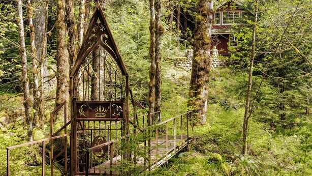 A forested area with a metal gate leading to a wooden bridge and a red building in the background. - Waterfront lodge on 24 acres with patio & fireplace (Rhododendron)