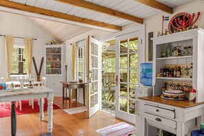 A room with a wooden ceiling, a dining table, a kitchen area with a water dispenser, and a view of a deck. - Waterfront lodge on 24 acres with patio & fireplace (Rhododendron)