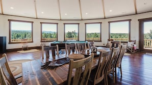 Un comedor con mesa de billar, sillas de madera y amplios ventanales con vistas a un paisaje boscoso.