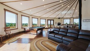 Amplia sala de estar con mesa de billar, sofá de cuero y grandes ventanales con vistas al exterior.