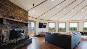 Un amplio salón con chimenea de piedra, un sofá modular grande y ventanas que ofrecen vistas al exterior.