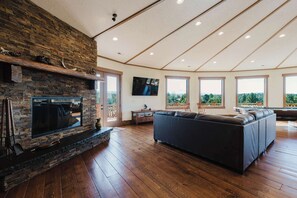 Ein geräumiges Wohnzimmer mit Kamin aus Stein, einer großen Eckcouch und großen Fenstern mit Blick ins Freie.