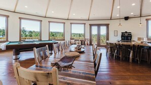 Amplio espacio interior con mesa de billar, mesa de comedor y sillas, con ventanas grandes y vistas al exterior.