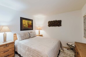 A bedroom with a bed, two bedside tables with lamps, a wall-mounted picture, and a small wooden dresser. - 3BR Townhouse Near SHARC & Village - Dog Friendly (Sunriver)