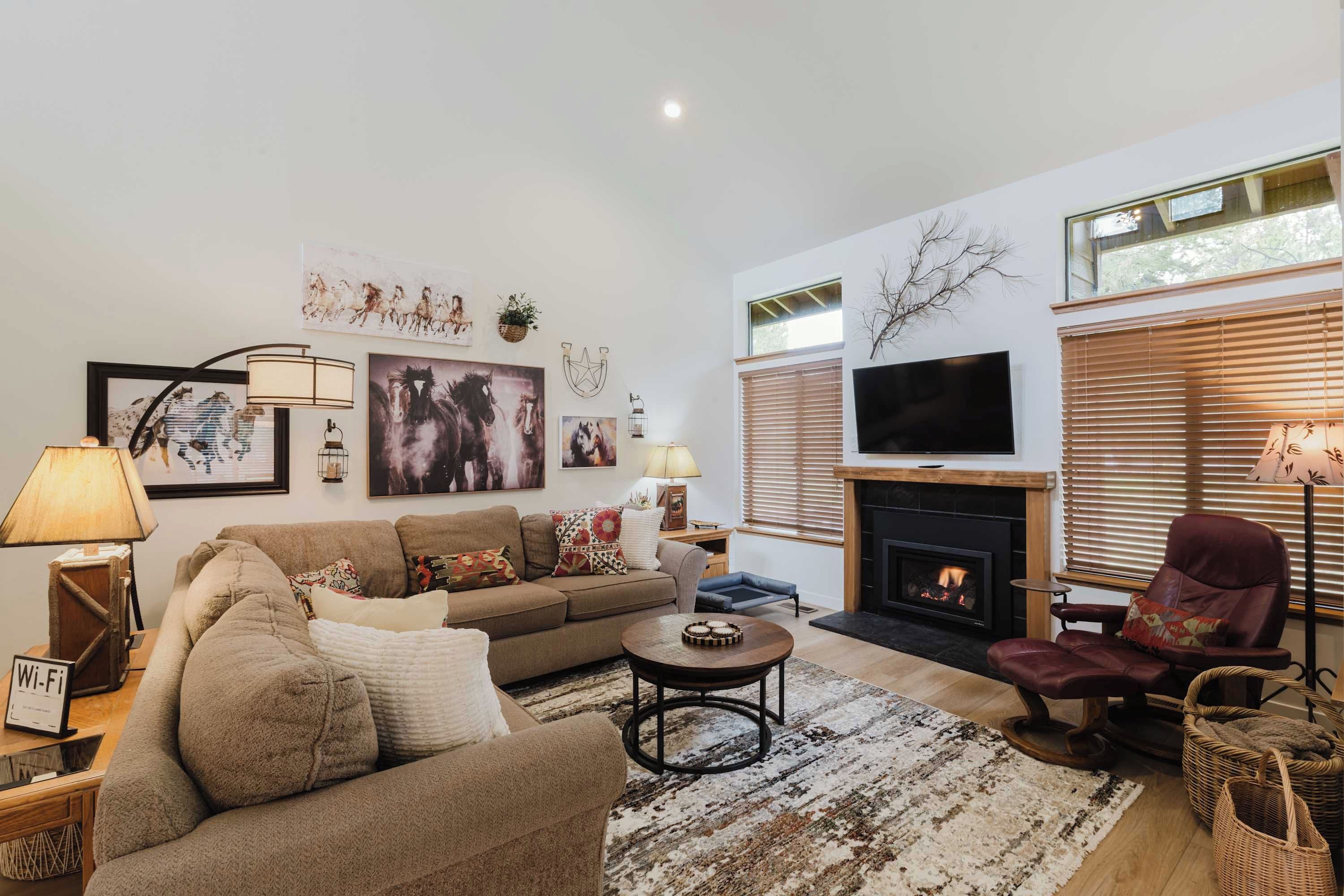 Una sala de estar con sofá, sillón, chimenea, televisión y obras de arte en la pared.