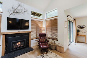 A living room with a fireplace, a television, a leather chair, and large windows.
