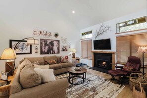 Una sala de estar con sofá, sillón, chimenea, televisión y obras de arte en la pared.