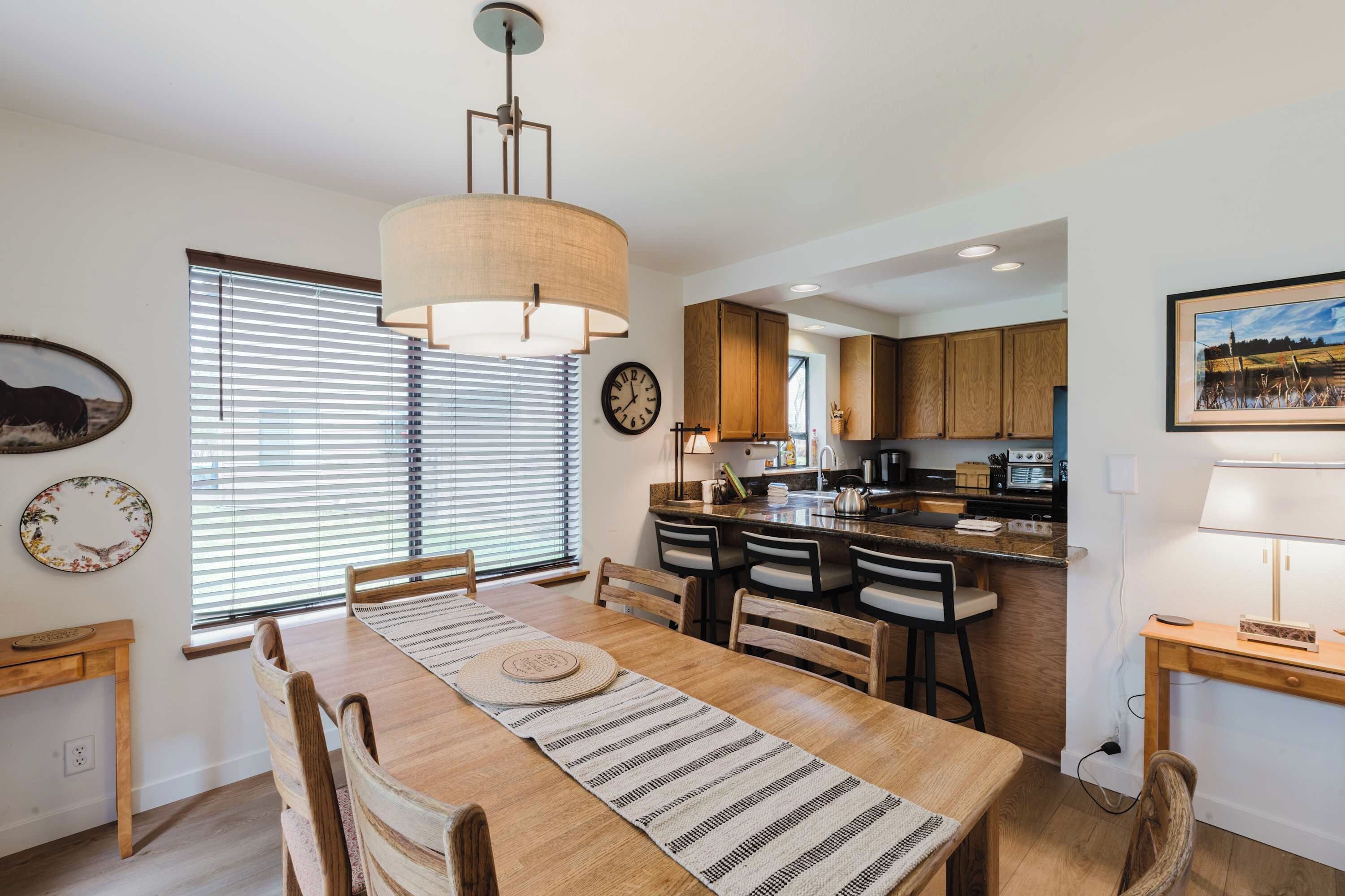 A modern kitchen with wooden cabinets, a dining table with chairs, and a hanging light fixture.