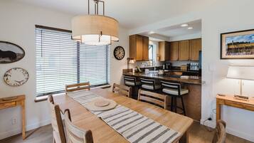 A modern kitchen with wooden cabinets, a dining table with chairs, and a hanging light fixture.