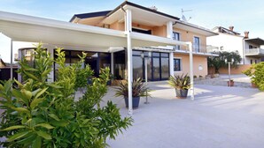 A modern two-story building with a covered outdoor area, potted plants, and a clear sky. - Premium Stay With Terrace and BBQ (Umag)