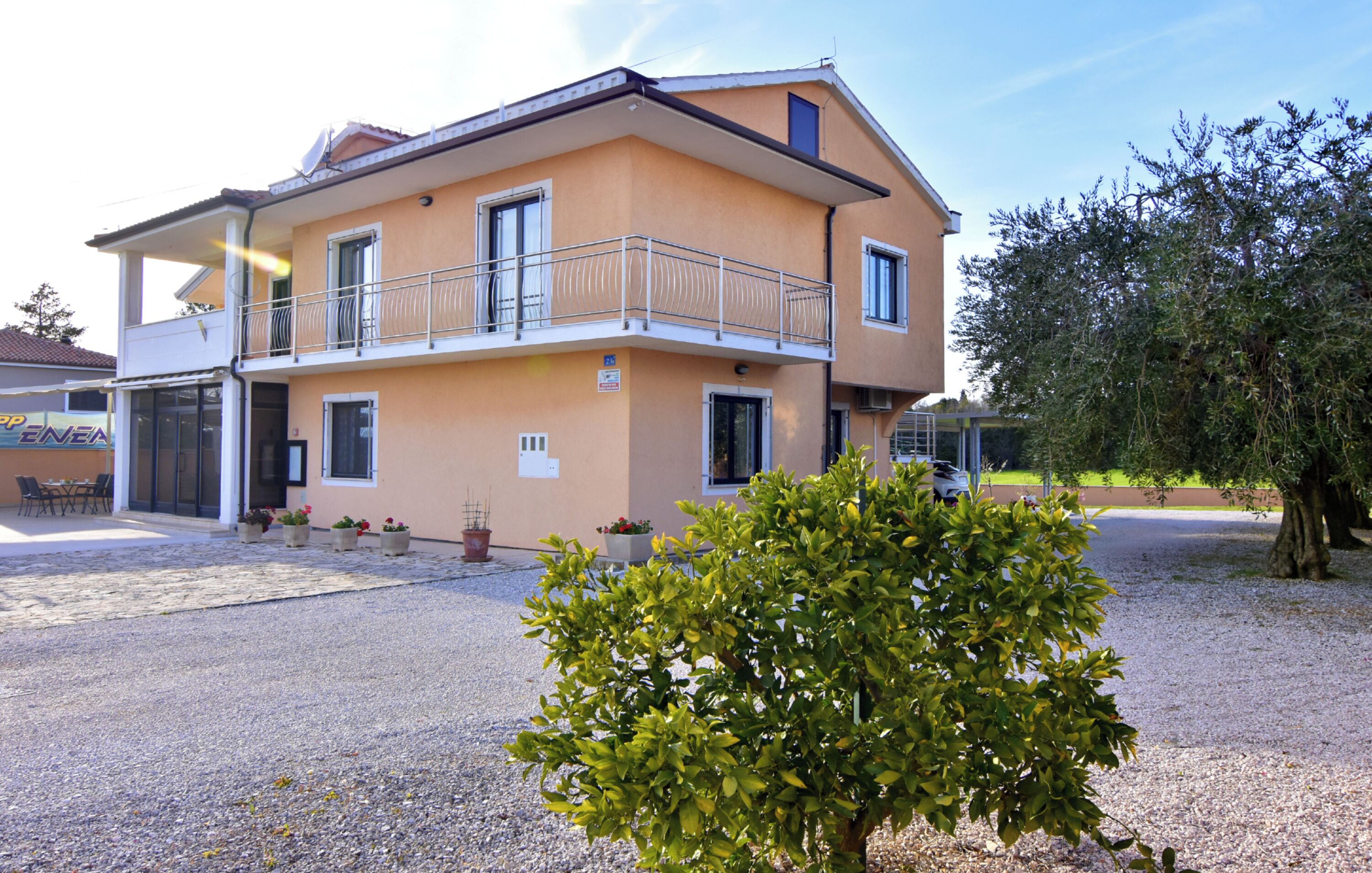 A two-story building with a balcony, a gravel driveway, and potted plants.