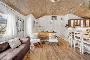 Ein modernes Interieur mit Holzboden, einem braunen Ledersofa, einem Essbereich mit weißen Stühlen und einer Küche mit Holzschränken.
