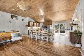 Eine moderne Küche mit Holzschränken, einem Essbereich mit weißen Stühlen und einer Wand mit Steinakzenten.