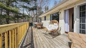 A wooden deck with outdoor furniture, including a rocking chair and a sofa, and a covered area with a grill.