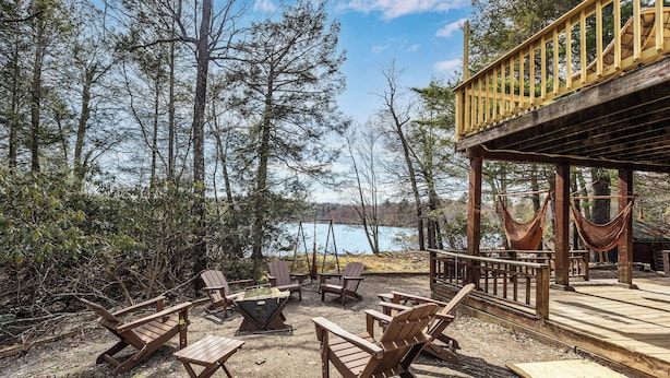 A deck with wooden chairs and a swing, overlooking a lake.