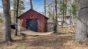 A red wooden shed with a black door, surrounded by trees and a hammock.