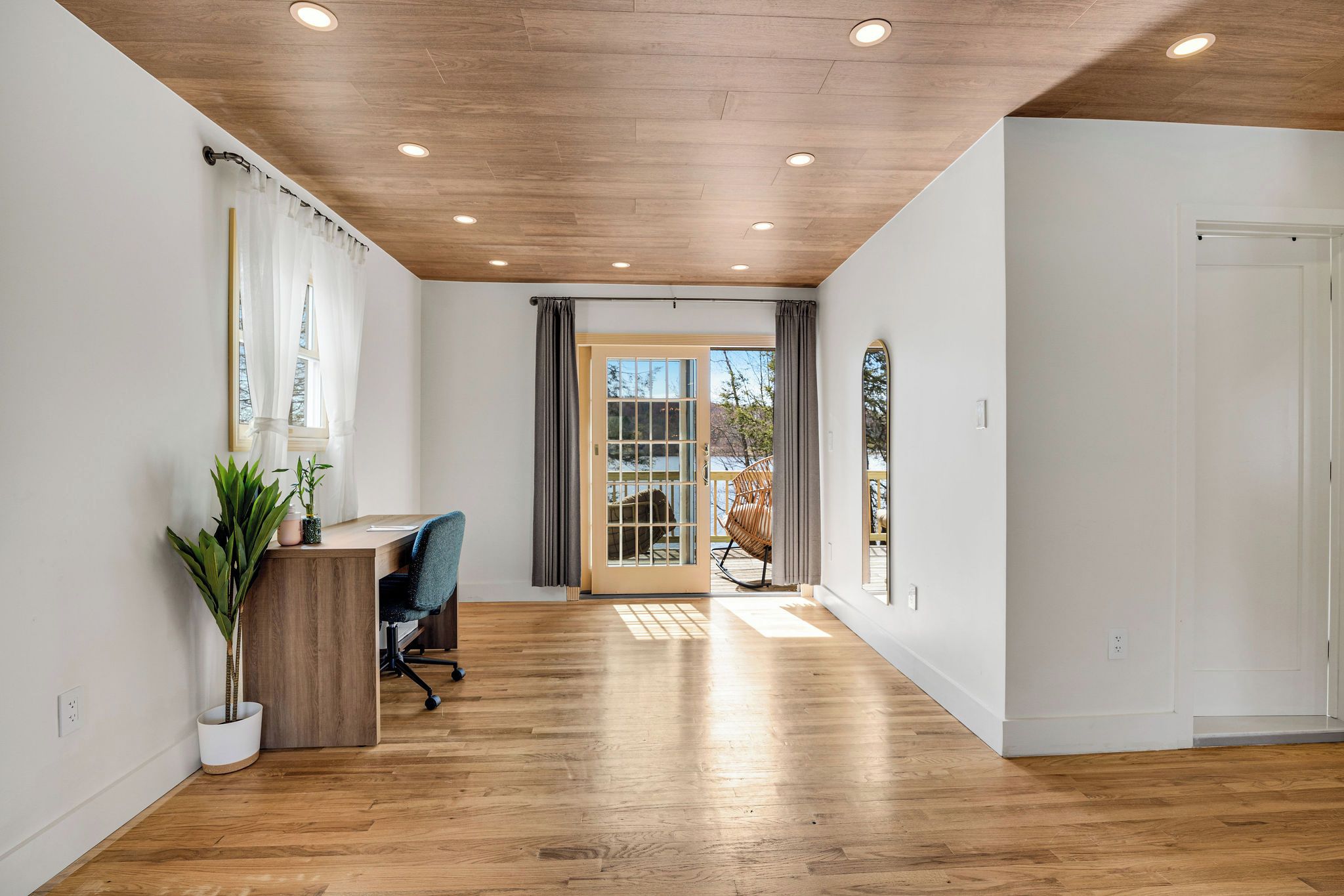 Una habitación amplia con suelo de madera, un escritorio con silla, una planta en maceta y un ventanal corredero que da a un espacio exterior.