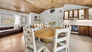 A spacious dining area with a wooden table and white chairs, a kitchen with wooden cabinets, and a ceiling with wooden beams.