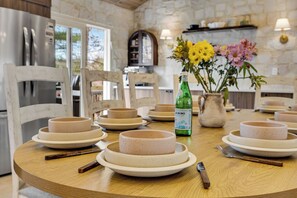 A round wooden table with ceramic plates and bowls, a bottle of Acronino, and a vase with flowers.
