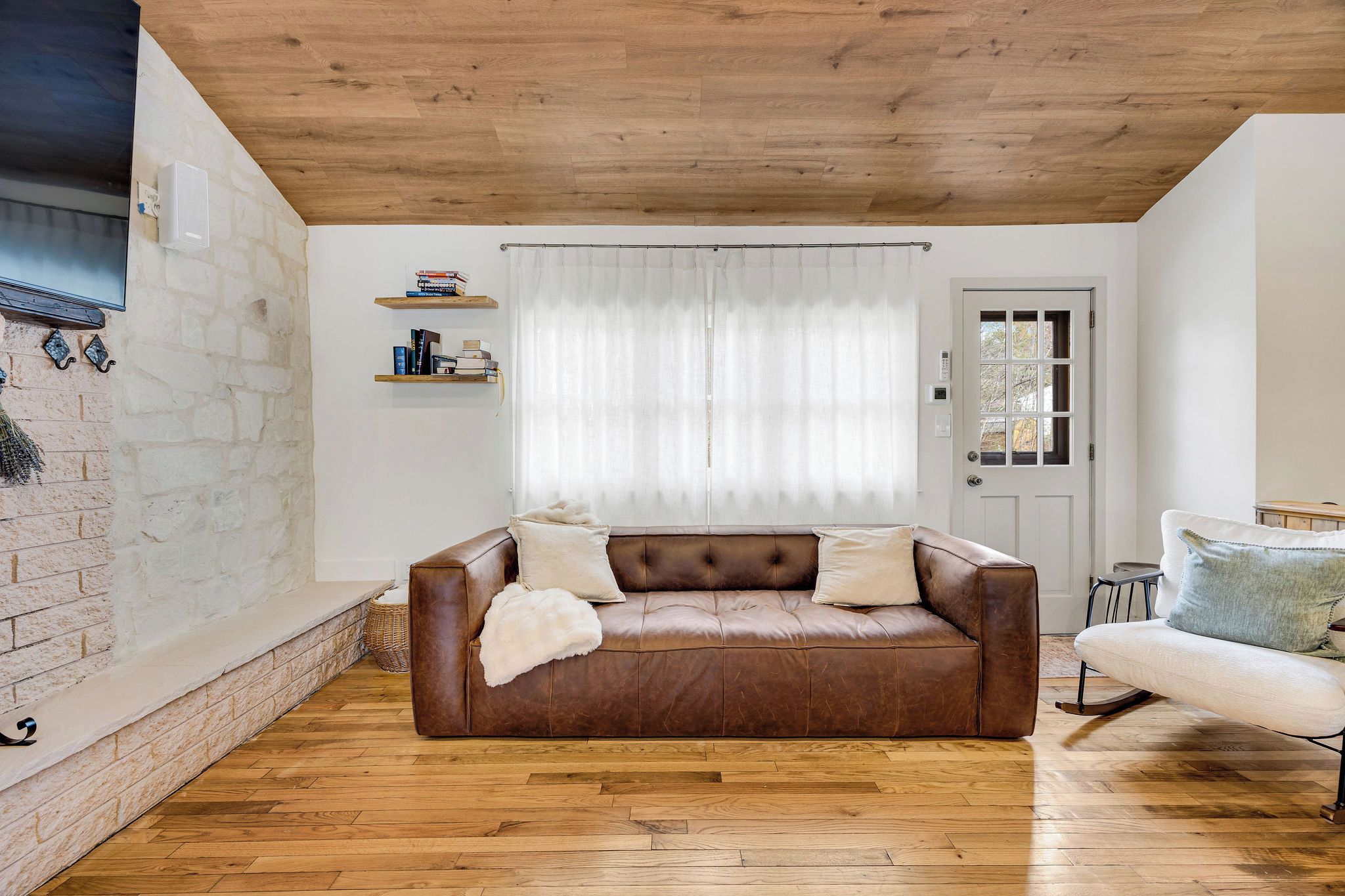 Un salon avec un canapé en cuir marron, une porte blanche et une fenêtre ornée de rideaux légers.