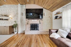 Ein Wohnzimmer mit Kamin aus Stein, Holzböden, einem braunen Ledersofa und einem Fernseher, der über dem Kamin angebracht ist.