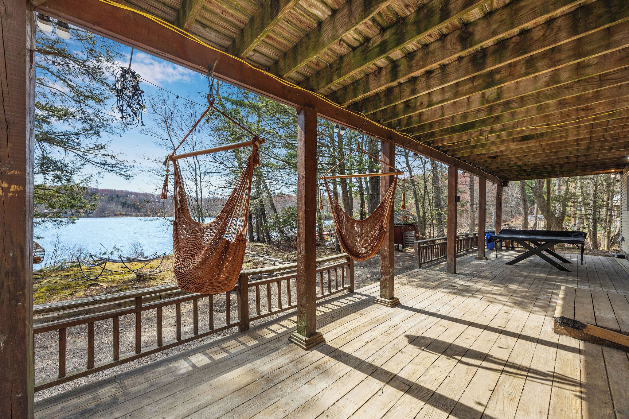 A wooden deck with two hammocks, a picnic table, and a view of a lake.
