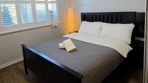 Een slaapkamer met een bed, nachtkastje en een raam met zonwering.