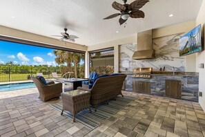 Eine Außenküche mit Steinrückwand, Deckenventilator und Blick auf einen Pool.