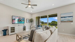 A living room with a sofa, TV, ceiling fan, and a view of the outdoors. - Eagle Trace Birdie: Water Park, Golf View, Near Disney (Kissimmee)