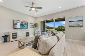 Ein Wohnzimmer mit Sofa, Fernseher, Deckenventilator und Blick ins Freie.