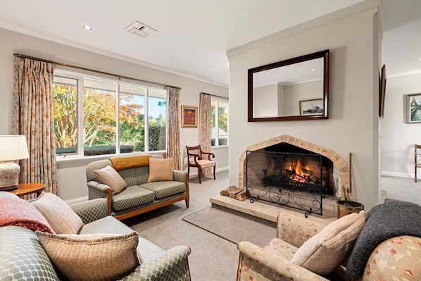 A living room with a fireplace, sofas, and a large window with curtains. - Wingana Homestead - Scenic Views, Bundanoon (Wingecarribee)