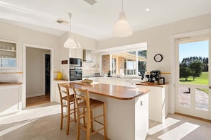 A modern kitchen with a central island, pendant lighting, and a view of the outdoors. - Wingana Homestead - Scenic Views, Bundanoon (Wingecarribee)