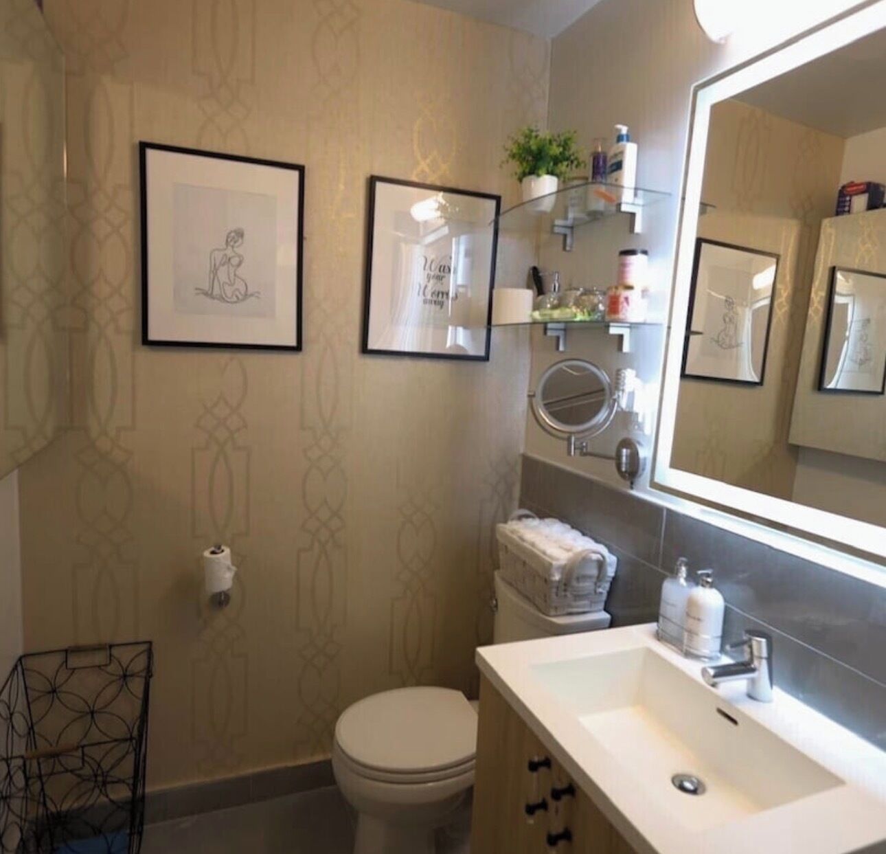 A bathroom with a toilet, sink, mirror, framed artwork, and a towel rack.
