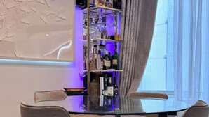 Un coin bar avec une table en verre et deux chaises, une étagère avec des bouteilles et une fenêtre avec des rideaux.