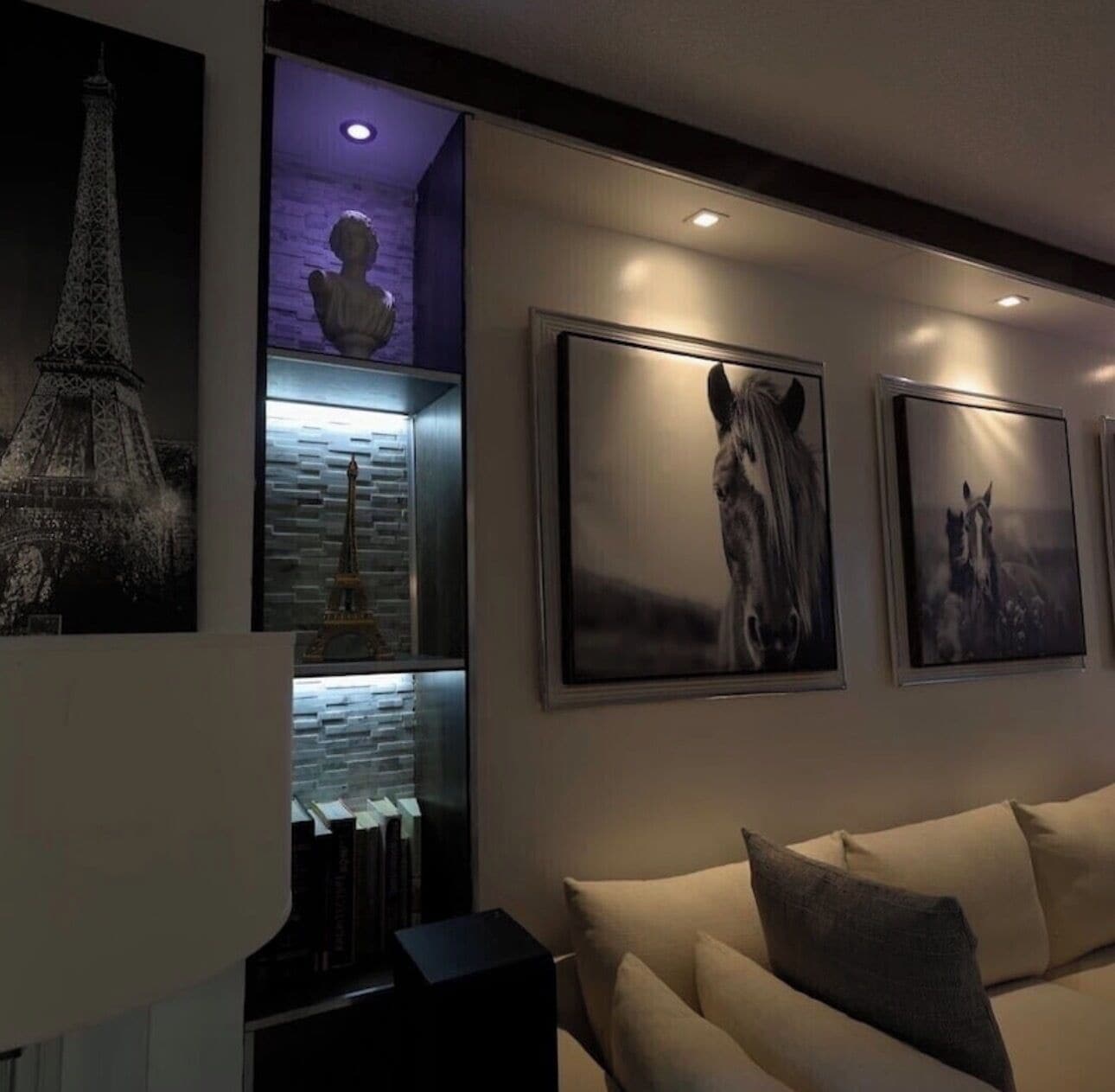 Un salón con sofá, estantería y obras de arte colgadas en la pared, incluyendo un caballo y la Torre Eiffel.