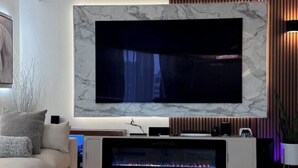 Un salon moderne doté d’un grand téléviseur à écran plat fixé sur un mur de marbre, d’un canapé, d’une cheminée et d’une console au design minimaliste.